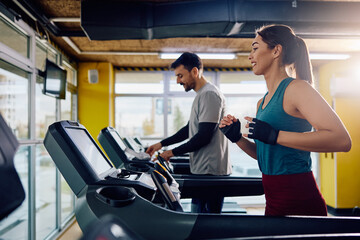 Happy athletic woman running on treadmill in gym.