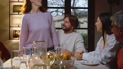 A young woman sits on her boyfriend's lap and announces to the rest of the family that they are getting married, showing everyone her wedding ring. The excited family hugs them