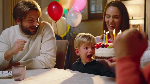 The family celebrates the toddler's birthday with a surprise, bringing a birthday cake with colored candles.
the child is delighted to blow out the candles.