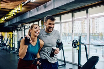 Cheerful athletic couple laughs while having sports training in gym.