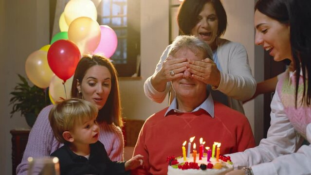 The family celebrates grandfather's birthday with a surprise, bringing a birthday cake with colored candles.
Grandfather blows out candles with his little grandson.