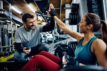 Cheerful athletic woman giving high five to her coach during weight training in gym.