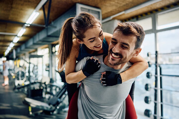 Playful athletic couple piggybacking during sports training in gym.