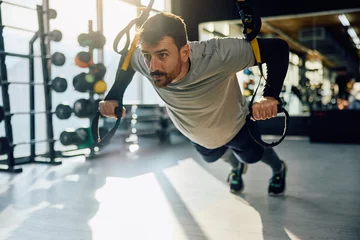 Fotobehang Athletic man using suspension straps while exercising strength in gym. © Drazen