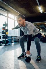 Male athlete using kettlebell during strength training in gym.