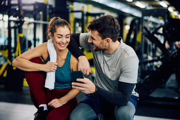 Fototapeta na wymiar Happy couple of athletes using smart phone in gym.