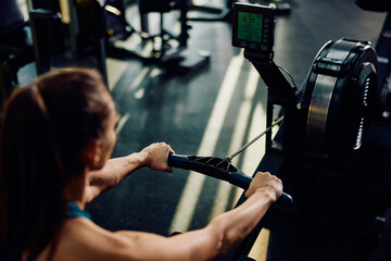 Close up of athletic woman using rowing machine while working out in gym. - obrazy, fototapety, plakaty