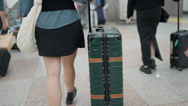 Back view of woman traveler walking and dragging a suitcase in airport. Female tourist walking and pulling luggage. Passengers in the airport. Travel concept
