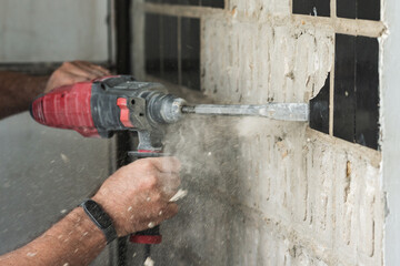Builder with a puncher dismantles old tiles from a concrete wall