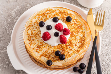 A large stack of delicious pancakes with sour cream and fresh berries on a white serving tray. Concept of traditional spring festival in Russia.