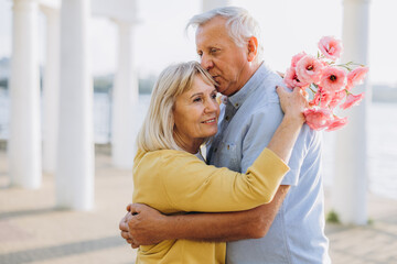 Senior couple with bouquet pink flowers on the background of the old architecture