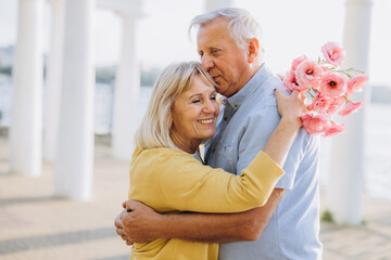 Senior couple with bouquet pink flowers on the background of the old architecture