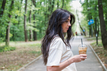 Woman walking in the summer park ,drinking coffee 