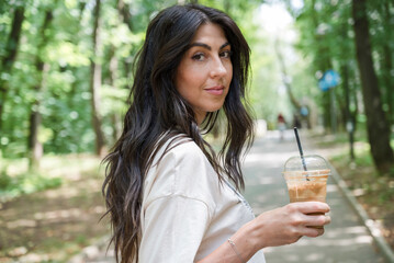 Woman walking in the summer park ,drinking coffee 