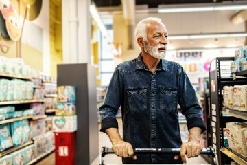 A gray-haired pensioner in a grocery store chooses groceries. Senior customer buying in supermarket. - obrazy, fototapety, plakaty
