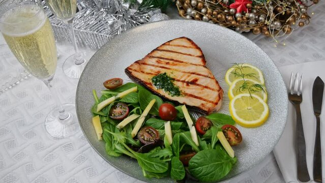 Grilled swordfish steak with fresh salad, tomatoes and cheese on a plate rotating. Christmas New Year decoration. Pour champagne into a glass. Close up