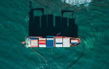 Aerial top down view of a container cargo ship stands aground after a storm with floating boom...