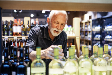 Smiling senior man choosing bottle of vine. Mature bearded happy male choosing bottle of vine in the supermarket.