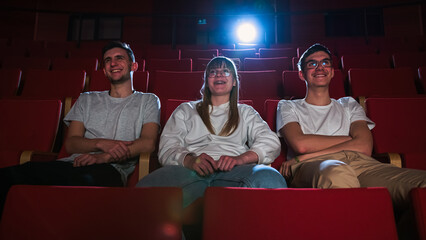 Three friends in the cinema hall, a girl and two boys having fun watching a film in the empty movie...