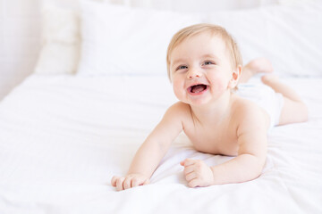 laughing or smiling baby boy blond with big eyes close-up or portrait in a crib at home, the concept of children's goods and accessories