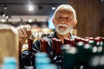 Positive male looking for perfect wine. Man choosing wine bottle picking up from alcohol shelf at...