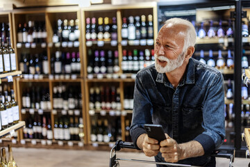 Mature male Caucasian consumer checking information on mobile phone in grocery. Man using cellphone...