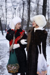 Two women with big braids in brown retro fur coats in winter street with snow. Winter cold weather....