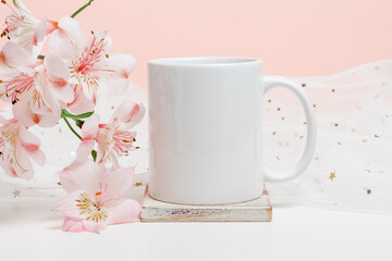 White mockup mug on wooden cup coaster with pink flowers and fabric with glitter. Mockup mug for logo, branding, print, gift and design.