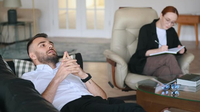 Lying down on the sofa. Man is on the therapy session with female psychologist.