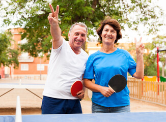 Mature couple showing victory near table tennis - Powered by Adobe