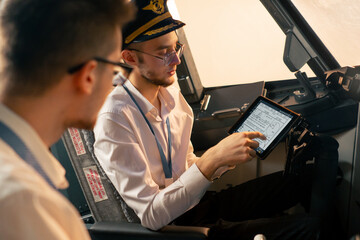 pilots in the cockpit of the plane near the control panel with a tablet in their hands discuss the route before the start of the flight simulator © Guys Who Shoot