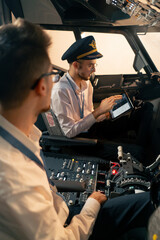 pilots in the cockpit of the plane near the control panel with a tablet in their hands discuss the...