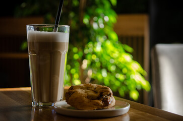 Latte in a tall transparent glass on a wooden cafe table, on a sunny day, a green tree in the...
