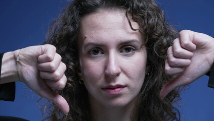 Woman giving thumbs down rejecting offer, close-up face of female person in 20s giving negative...
