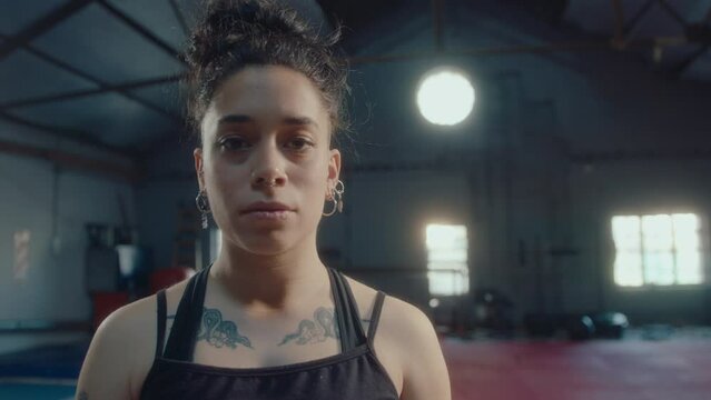 Young female athlete with undercut hairstyle, nose piercing and tattoos on body wearing sportswear standing in gym and posing for camera with confidence. Handheld shot, video portrait