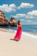 young latino woman in a pink long dress at the beach of algarve costa in Portugal