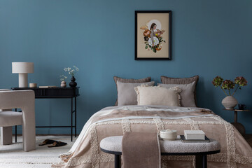 Warm and cozy bedroom with mock up poster frame, cozy bed, beige bedding, blue wall, pillows, wooden sideboard, bench, gray armchair, vase with flowers and personal accessories. Home decor. Template.	
