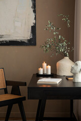 Minimalist composition of warm workspace interior with black desk, rattan armchair, candels, notebook and personal accessories. Template.