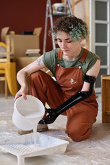 Vertical image of girl with prosthetic arm painting walls in the room