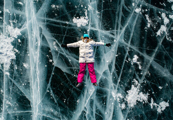 Aerial top down shot of the young woman lying on the blue cracked ice of Baikal and shaking hands...