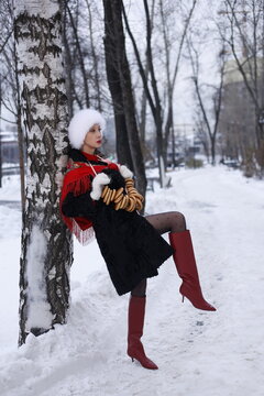 Woman with big braid in brown retro fur coat in winter street with snow. Winter cold weather. Girl with string bag and jumbles, in white fur gloves and in high red boots. Smile. Vintage, soviet time.