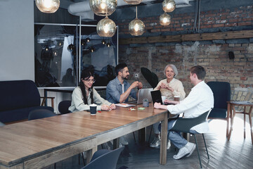 Group of young people discussing business while sitting in the creative office, while using...