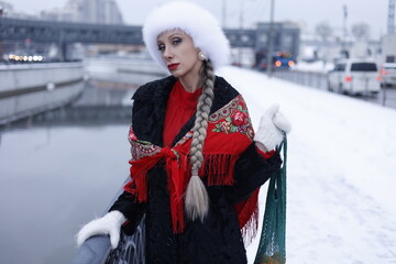 Woman with big braid in brown retro fur coat in winter street with snow. Winter cold weather. Girl...