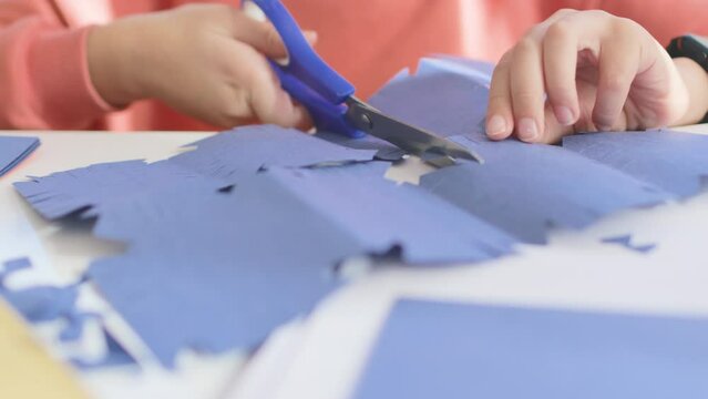 The child cuts from colored paper. a boy cuts a snowflake out of blue paper with scissors while sitting at the table. scissors close-up. children's creativity.