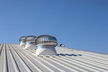 Ventilation fan on the roof. Three shiny metal rotating balls on industrial factory roof for circulating cool air into warehouse on blue sky background with selective focus. - obrazy, fototapety, plakaty