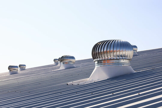 Ventilation fan on the roof. Shiny metal swivel on the roof of a factory or industrial plant to circulate and control cool air into the building on a blue sky background with selective focus.