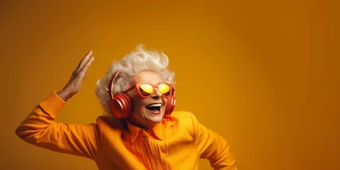 Foto auf Acrylglas Satisfied old woman with grey hair wearing bright headphones and clothes does best body moves energetically. Cheerful senior woman in bright sunglasses smiles broadly dancing to favourite song © EVGENIA