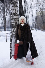 Woman with big braid in brown retro fur coat in winter street with snow. Winter cold weather. Girl...