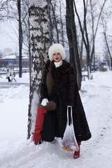 Woman with big braid in brown retro fur coat in winter street with snow. Winter cold weather. Girl...