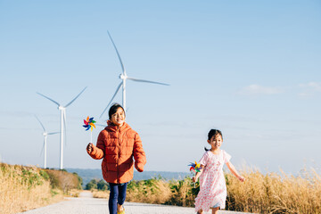 Two children girl with pinwheel happily near windmills. Family moments at turbines symbolize clean...